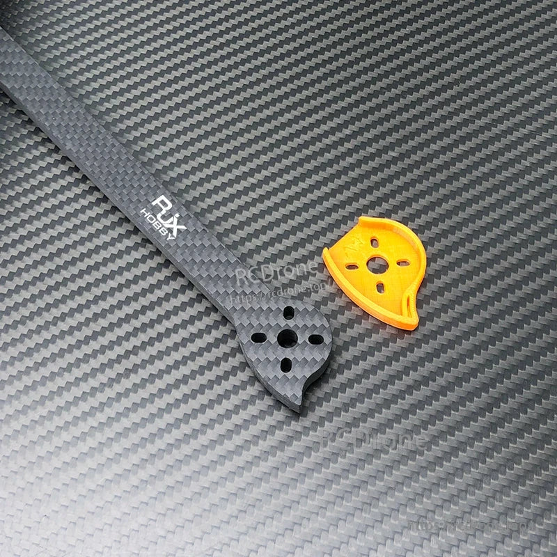 Close-up of an RJX carbon fiber FPV drone frame arm with motor mount holes and an orange mount plate