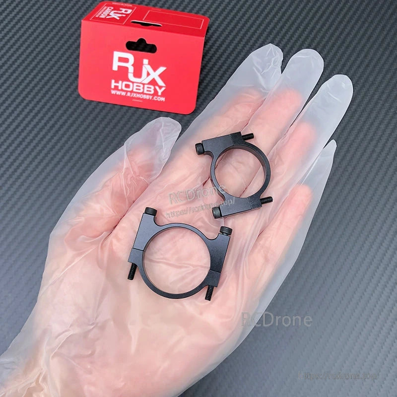 RJX Hobby black aluminum tube clamp bracket set with four screws, shown in hand beside retail box