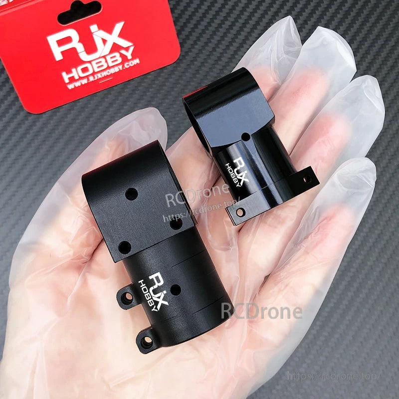 RJX Aluminum Landing Gear Tee Tripod Connector, Pair of black RJX Hobby aluminum landing gear tee tripod connectors held in a gloved hand against a carbon fiber background.