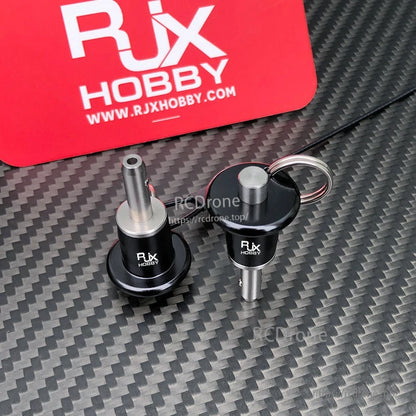 RJX Stainless Steel Ball Lock Pin, Two RJX Hobby stainless steel ball lock pins with black knobs and a pull ring on a carbon fiber surface