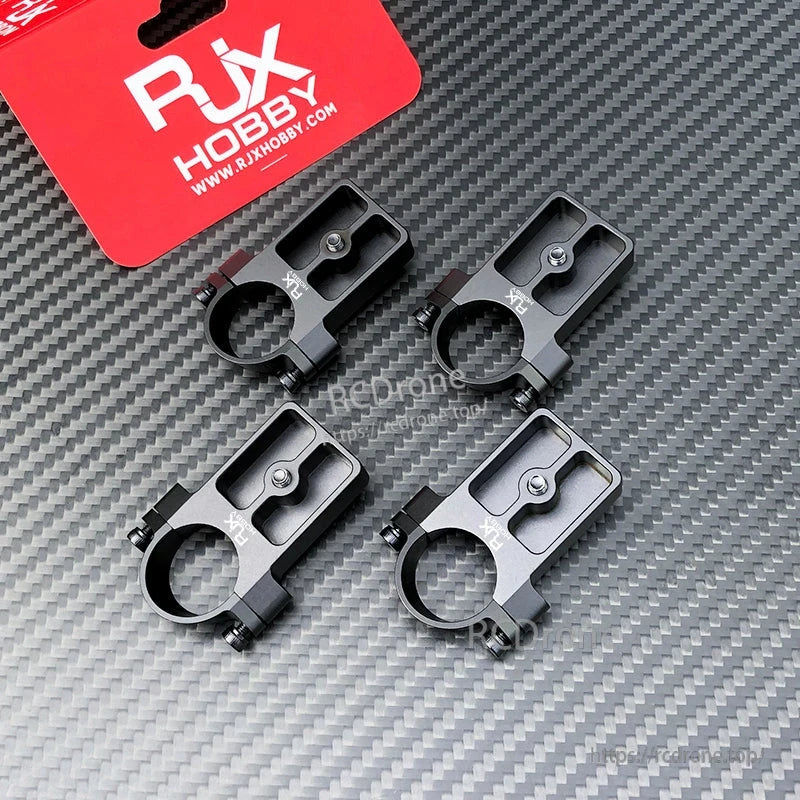 Set of four RJX UAV drone tube mounts, black aluminum clamps with screw fasteners on carbon-fiber background