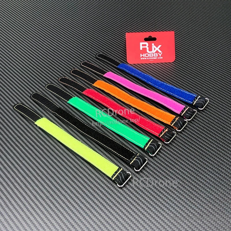 Assorted RJXHOBBY stitched silicone battery straps with metal buckles in multiple colors on a carbon-fiber surface