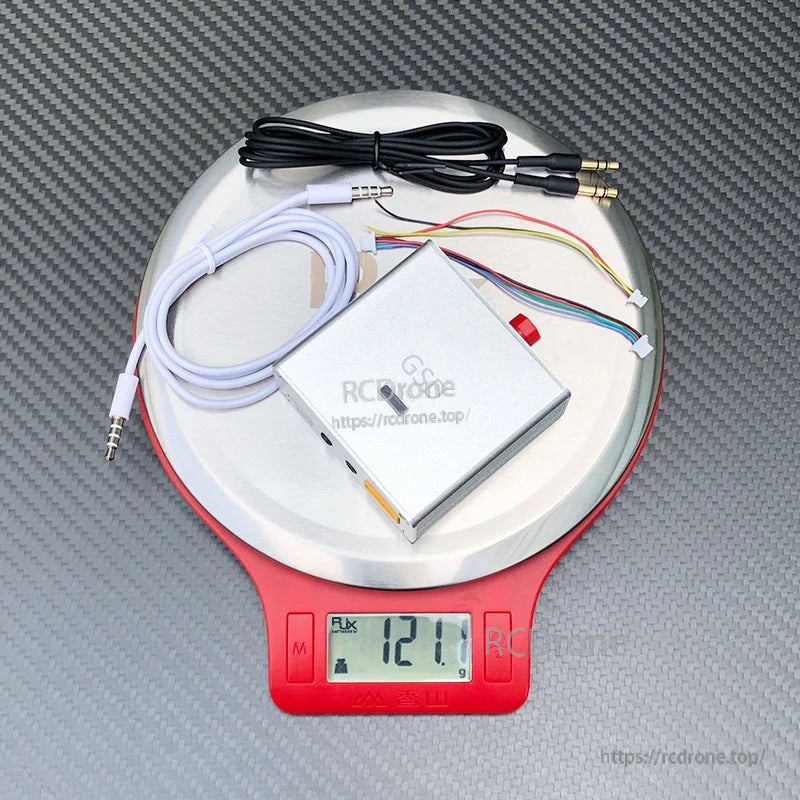 Metal-cased FPV data link module with wiring harness and 3.5mm cables on a digital scale reading 121.1g