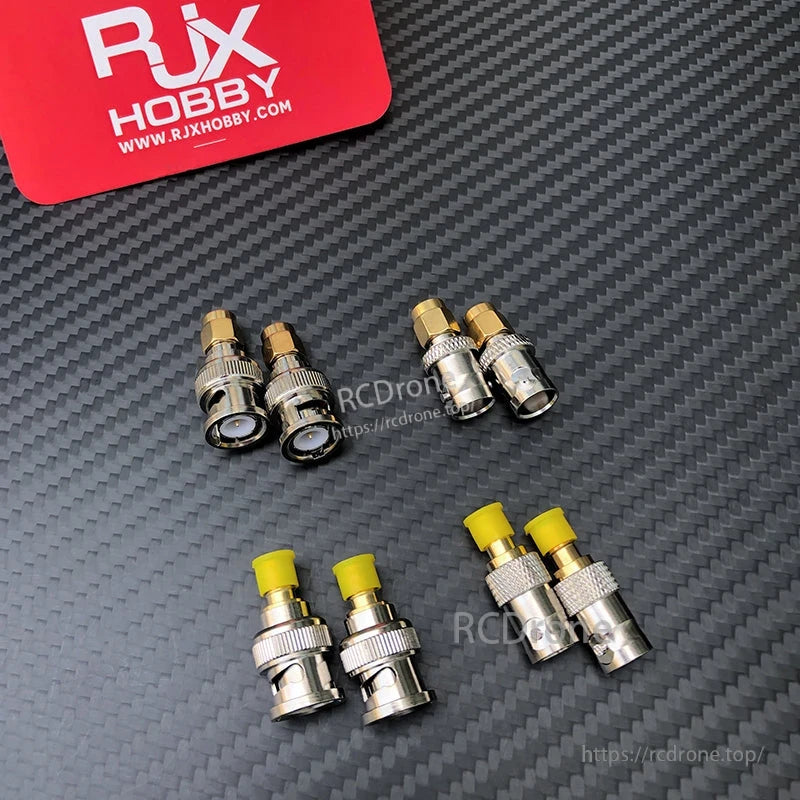 Four SMA to BNC RF coaxial adapters with gold-colored tips, arranged on a carbon-fiber background