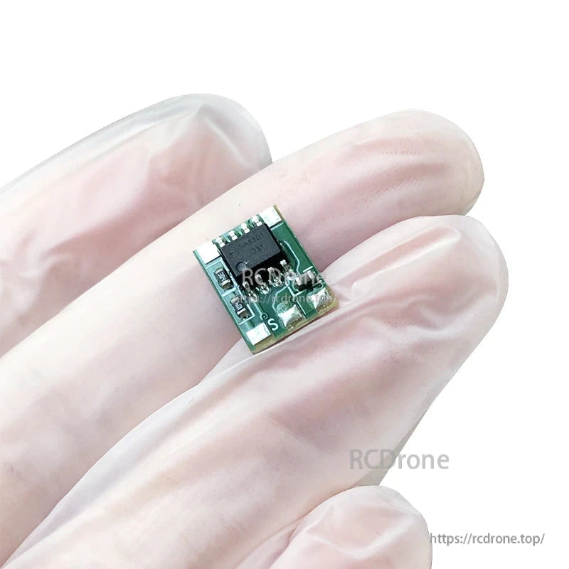 Micro brushed RC ESC motor drive module board held between gloved fingers, compact green PCB with S pad marking