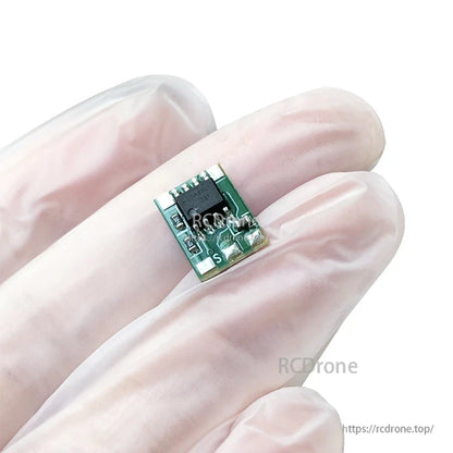 Micro brushed RC ESC motor drive module board held between gloved fingers, compact green PCB with S pad marking