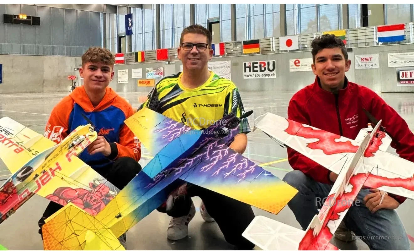 Three hobbyists holding colorful RC fixed-wing model airplanes inside an indoor flying hall
