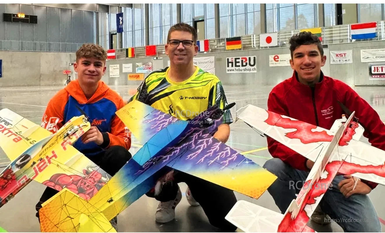 Three people holding colorful RC fixed-wing model airplanes indoors, with a yellow jet and two delta-wing models