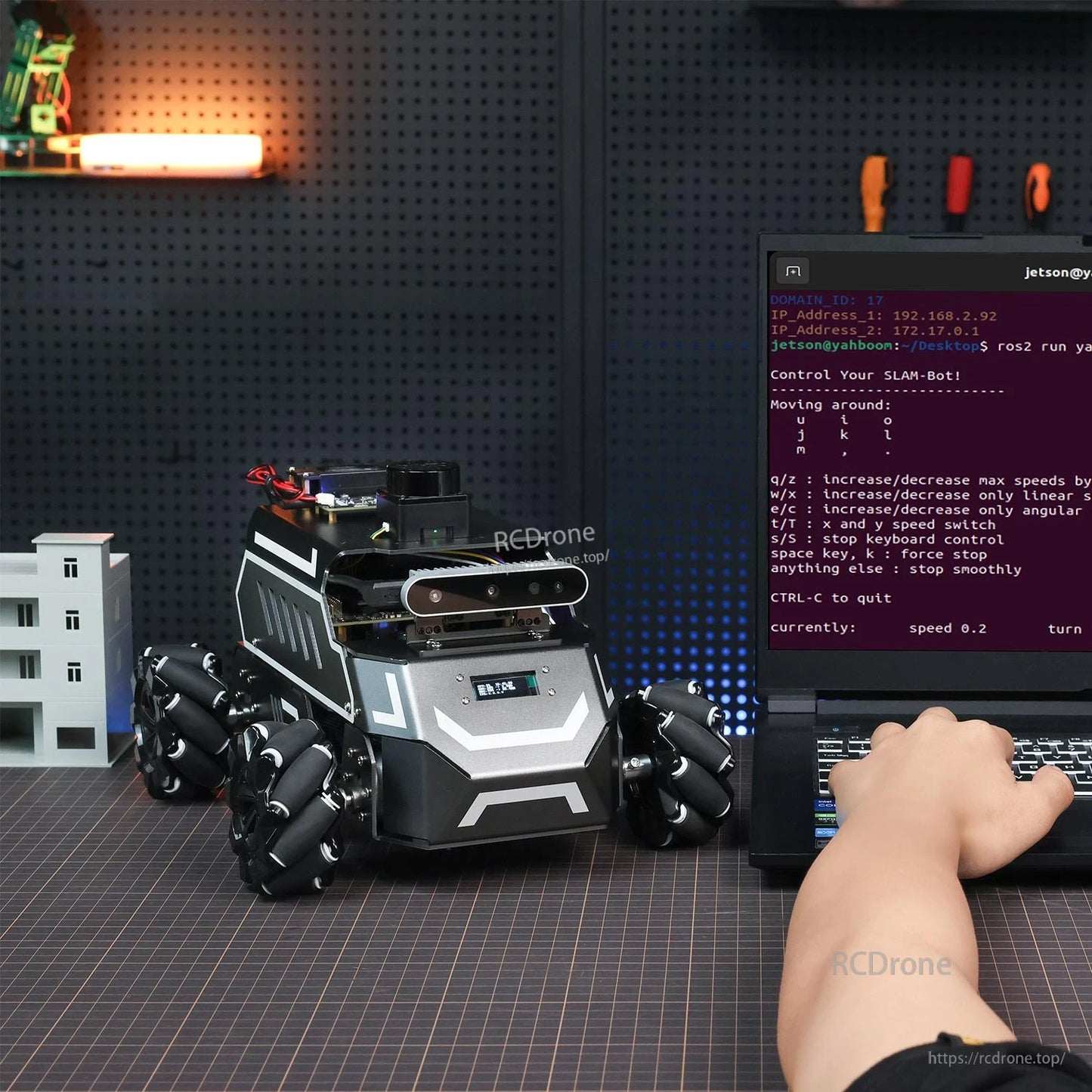 Robot on workbench next to laptop terminal showing keyboard control commands for SLAM and movement
