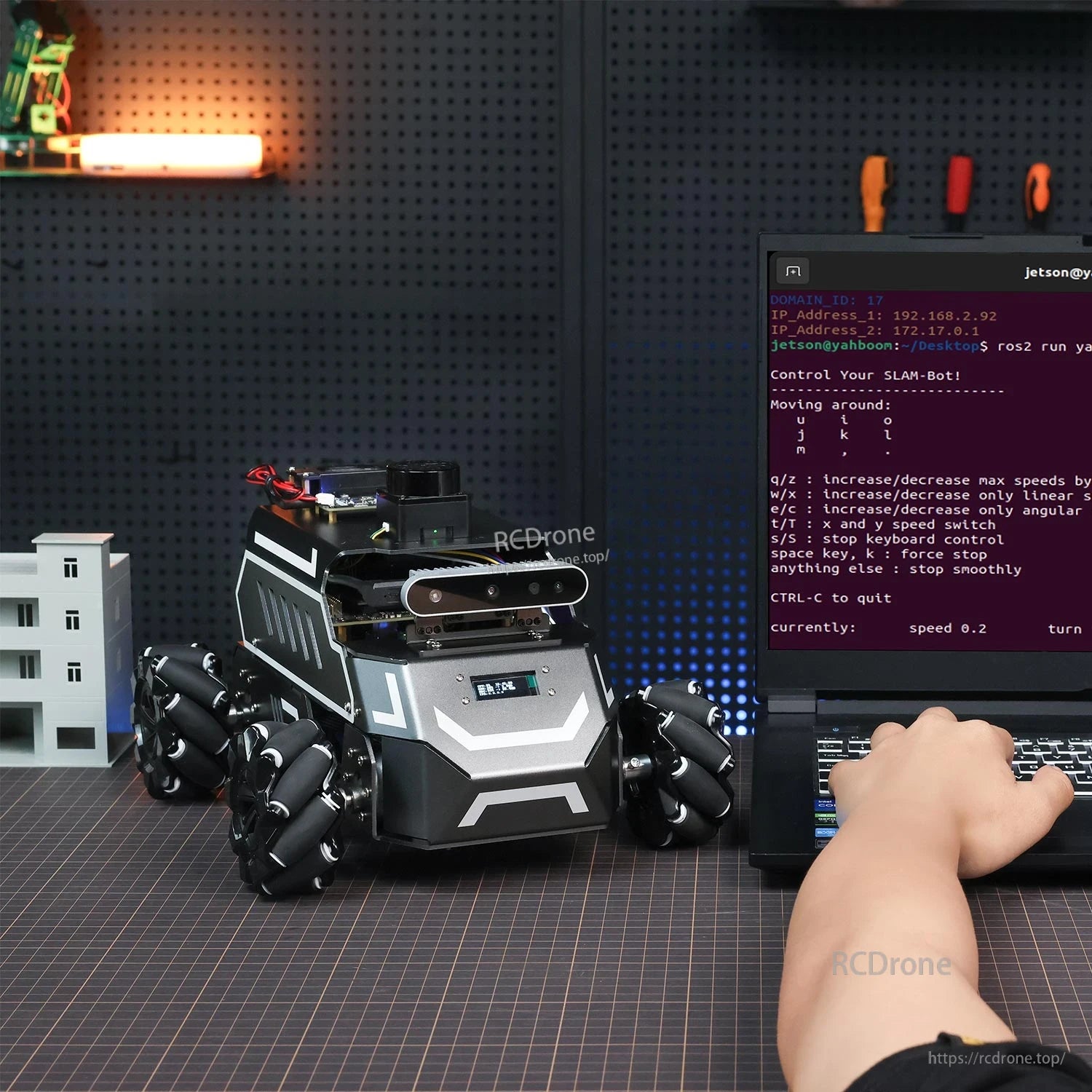 Robot on workbench next to laptop terminal showing keyboard control commands for SLAM and movement