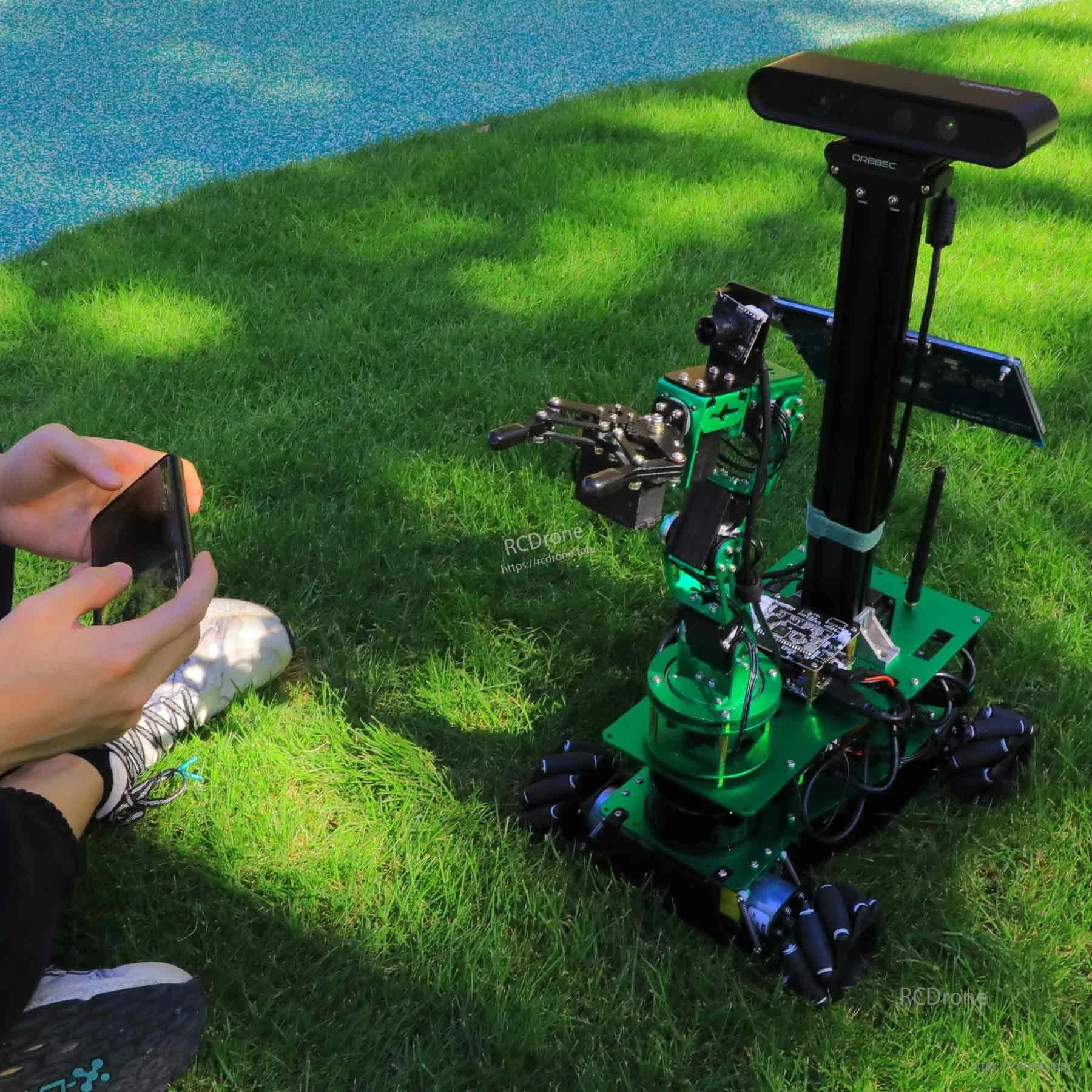 Yahboom ROSMASTER X3 PLUS ROS Robot on grass with robotic arm and sensor mast, user holding phone controller