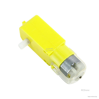 Angled close-up of TT DC motor showing white output shaft, yellow gearbox, and clear rear cover