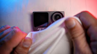 Flywoo Naked GoPro-style action camera module with front screen and lens, being wiped clean by hand