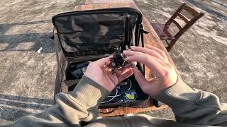 FLYWOO O4 1S 5V/3A BEC, Hands holding a small FPV quadcopter over an open backpack outdoors, with visible wiring and electronics